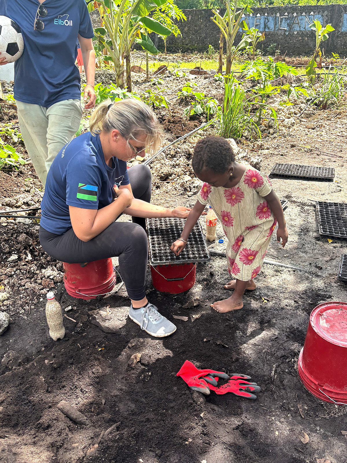 ElbOil employee and young girl planting seeds together during a community engagement project in Zanzibar, promoting environmental awareness and sustainable growth.